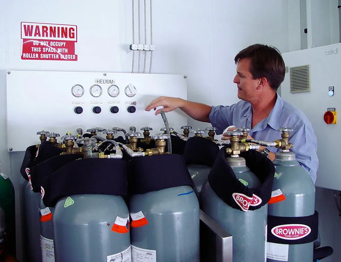 Technician adjusting a Trimix gas blending panel while monitoring gas mixtures in a well-lit workshop